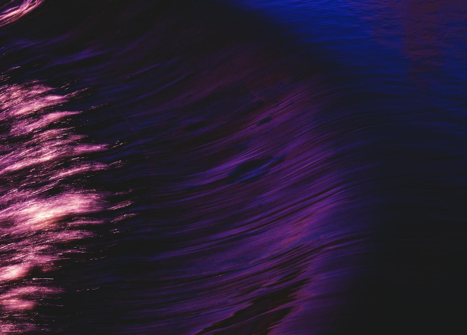 Swirling abstract art with vibrant purple and pink reflections in water, evoking a sense of motion and flow.